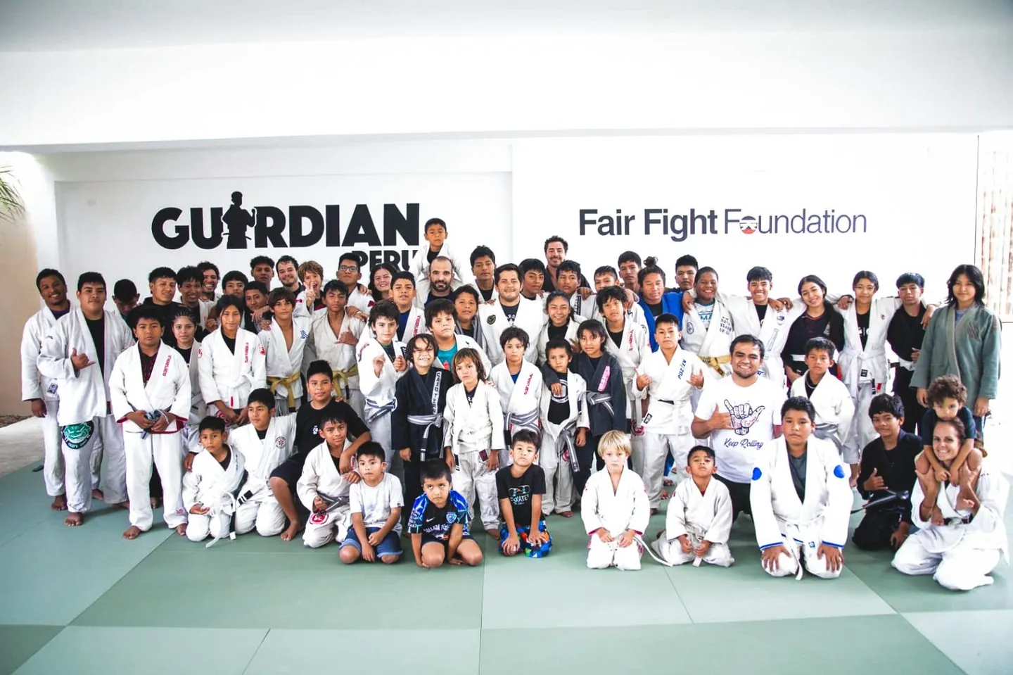 Students and coaches on the mats at Guardian Peru in Máncora, in front of the Guardian and Fair Fight Foundation logos